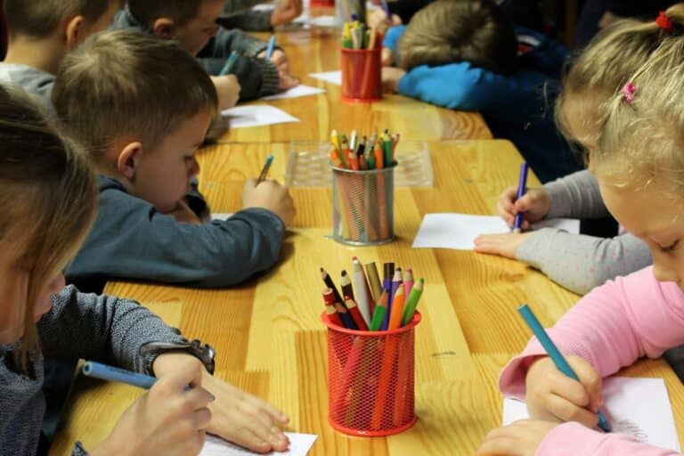 Crianças desenham juntas em uma mesa, exemplificando um ambiente de educação inclusiva e colaborativa.